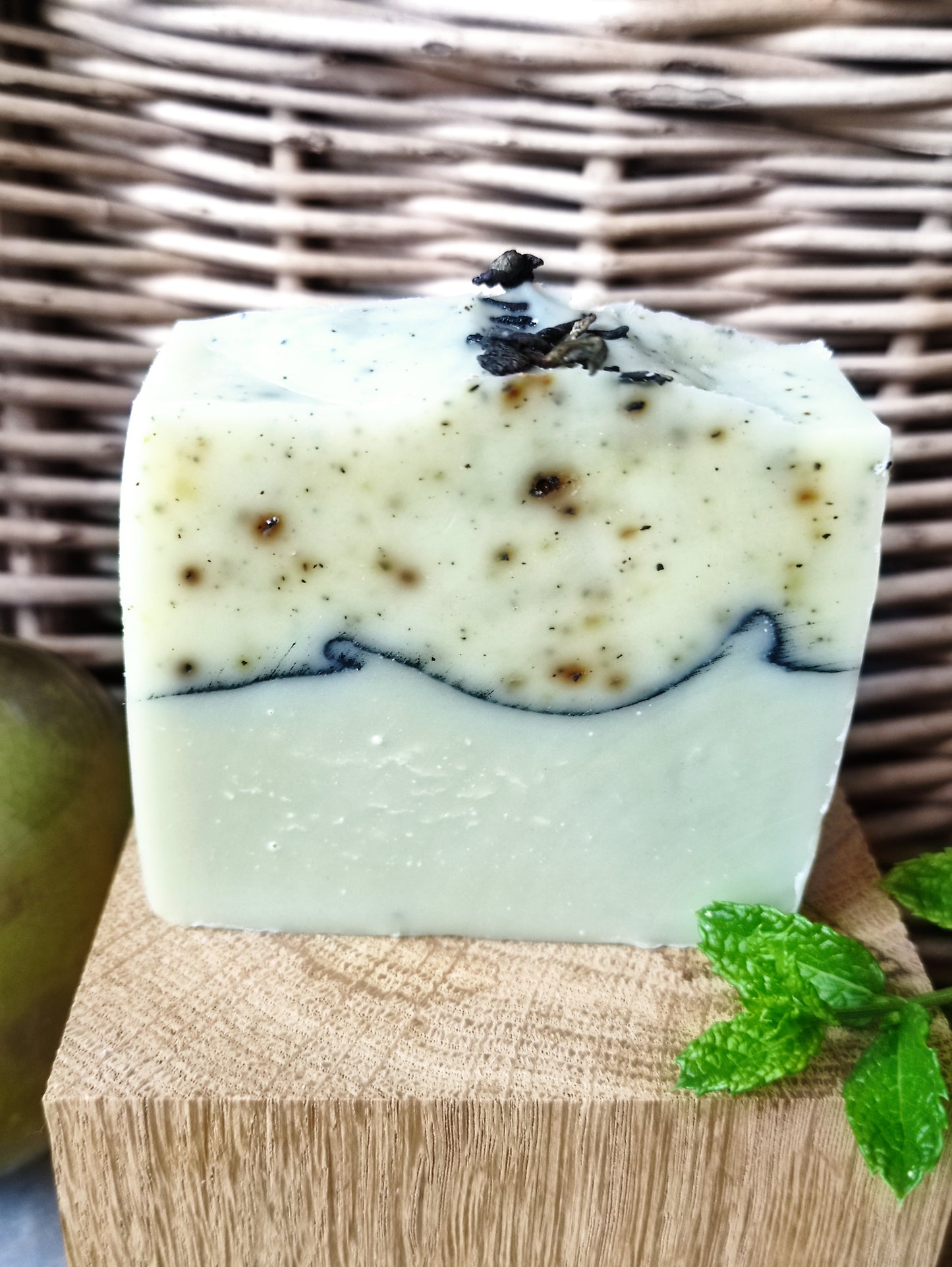 Savon artisanal saponifié à froid. Il est bicolore. La partie inférieure est vert clair et la partie supérieure blanche mouchetée de petits fragments de thé vert. une ligne de charbon sépare les deux parties.