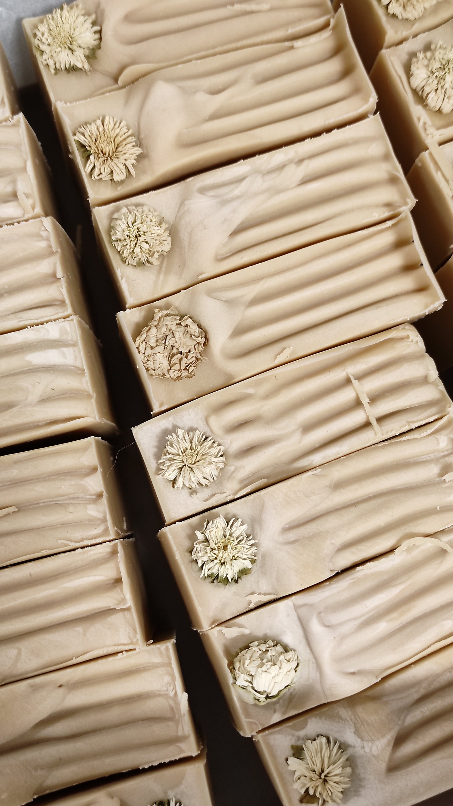 Savon artisanal saponifié à froid. Il est rose pâle avec ne fleur de camomille sur le dessus.