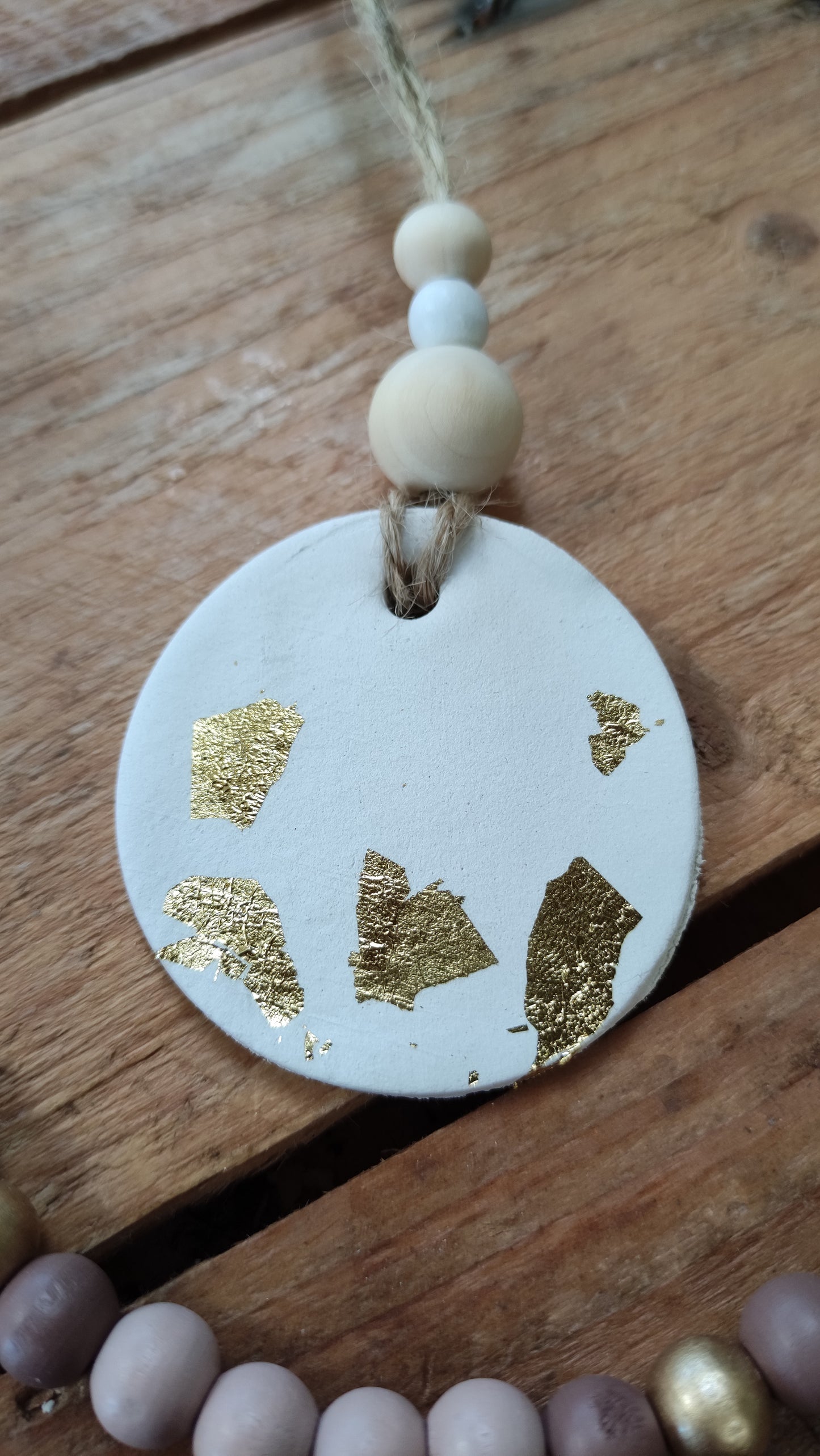 suspension ronde en argile blanche et touche de feuilles d'or soutenu par une ficelle de chanvre avec 3 perles de bois aux tons naturels