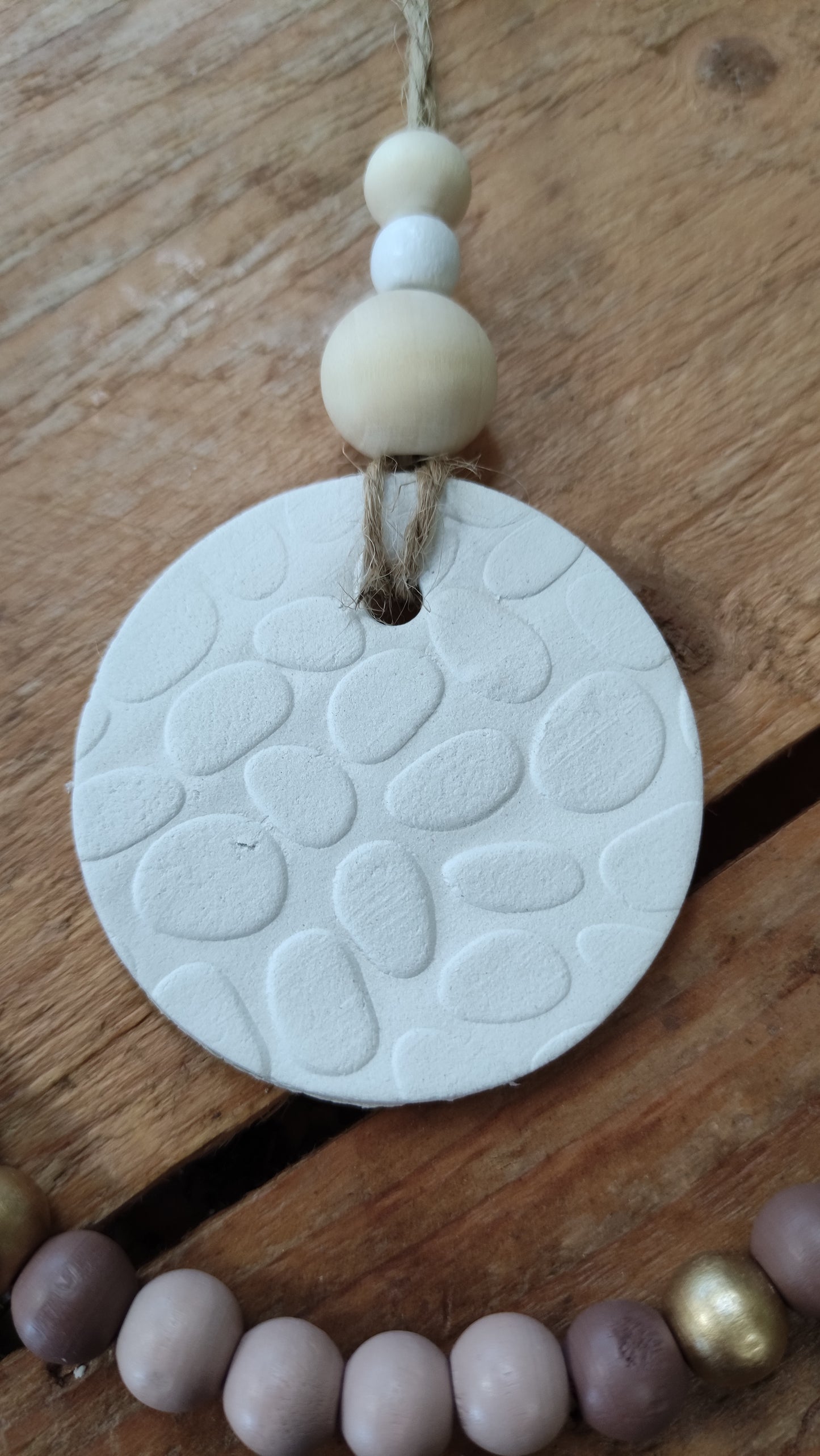 suspension ronde en argile blanche (motif galet en relief) soutenue par une ficelle de chanvre avec 3 perles de bois aux tons naturels
