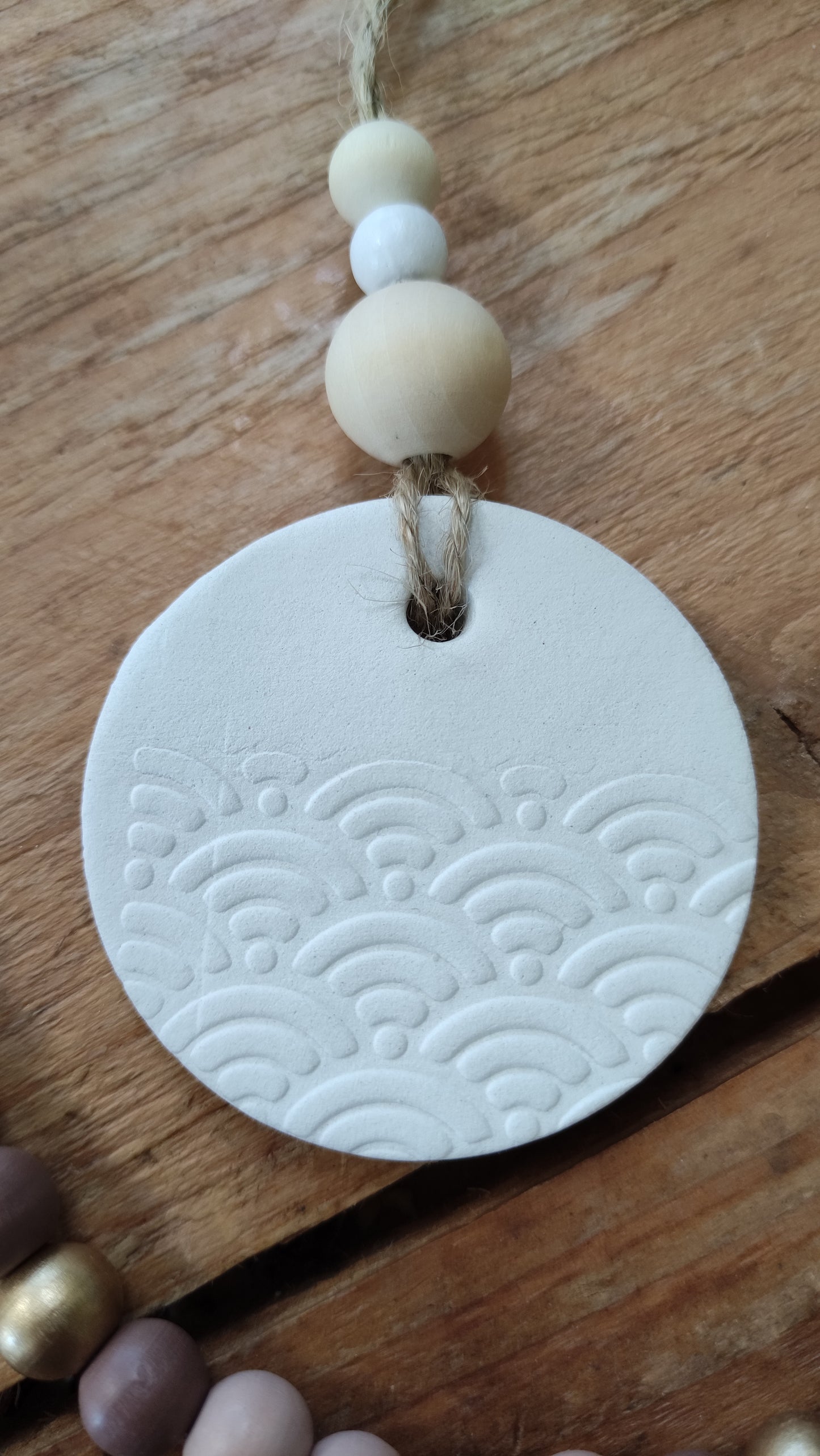 suspension ronde en argile blanche (motif vague en relief) soutenue par une ficelle de chanvre avec 3 perles de bois aux tons naturels