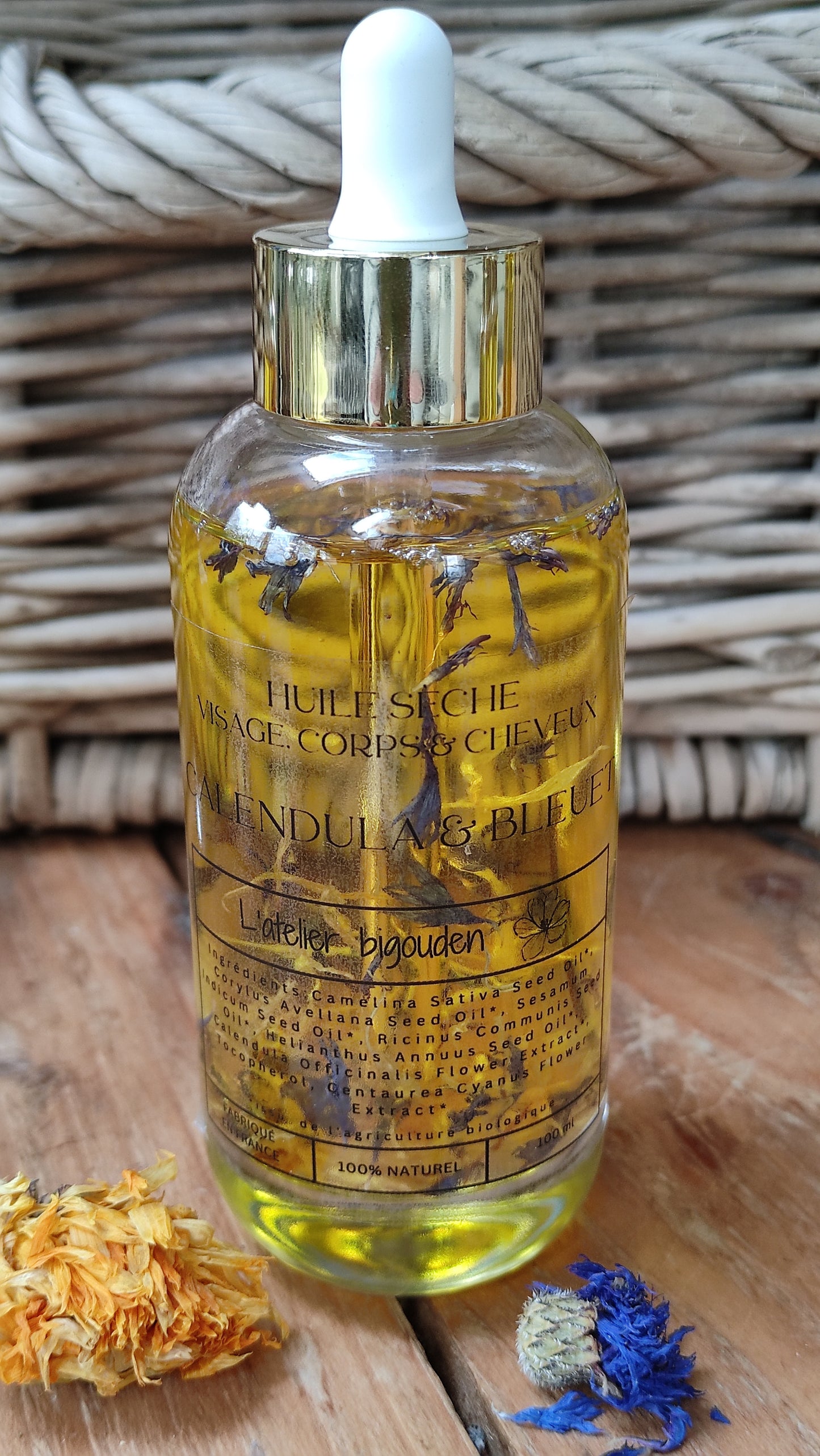 joli flacon en rondeur, transparent avec un bouchon compte-goutte doré. L'huile est jaune or avec des étale de fleurs de calendula et de bleuet en suspension.