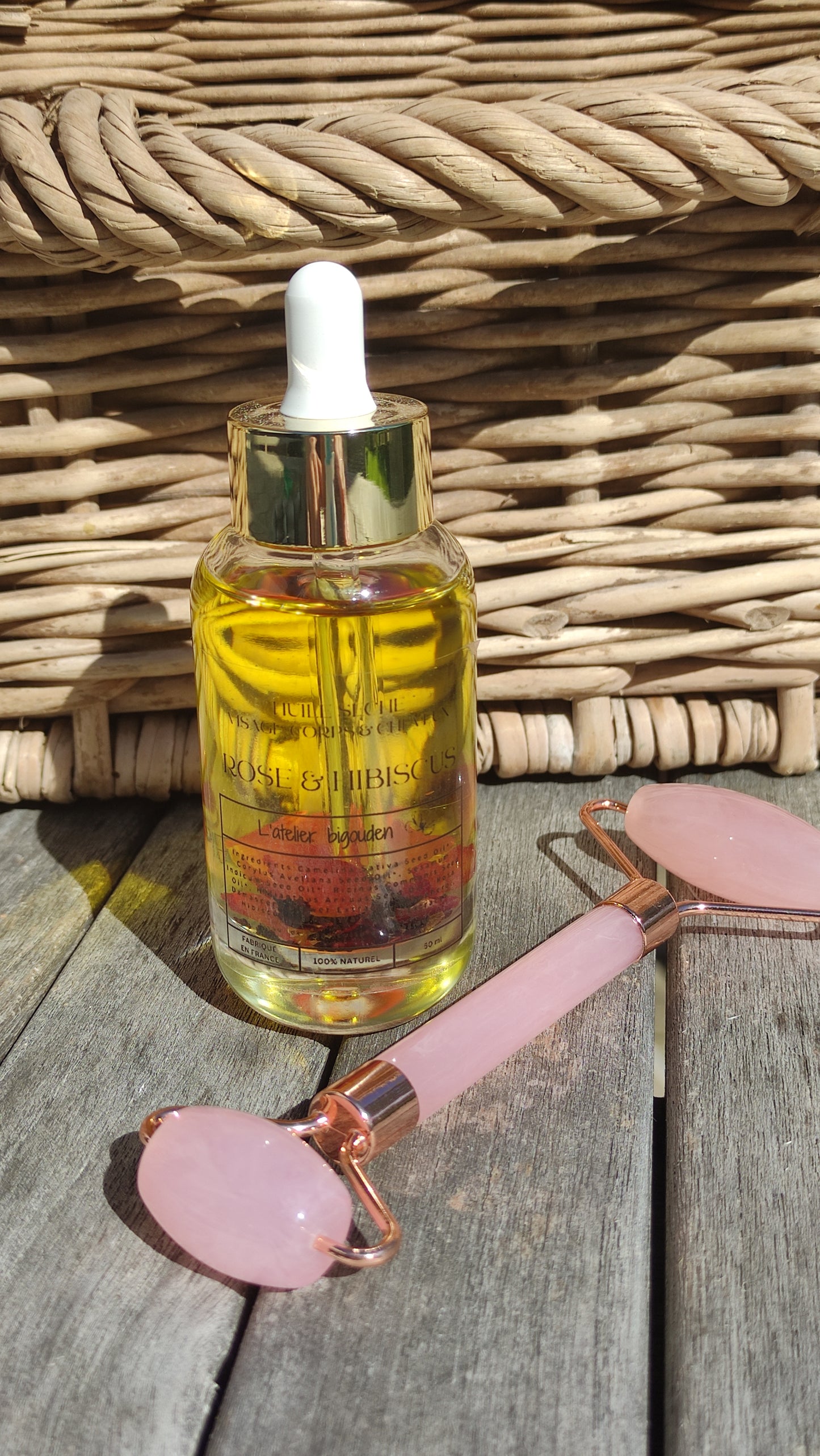 joli flacon en rondeur, transparent avec un bouchon compte-goutte doré. L'huile est jaune or avec des pétales de rose et des fleurs d'hibiscus en suspension.