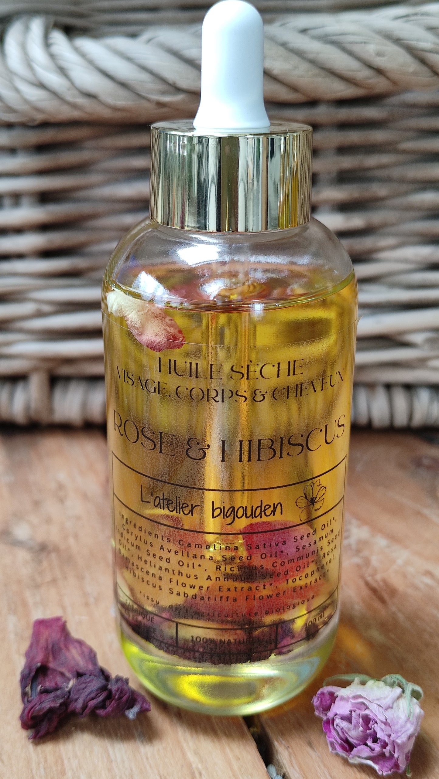 joli flacon en rondeur, transparent avec un bouchon compte-goutte doré. L'huile est jaune or avec des pétales de rose et des fleurs d'hibiscus en suspension.