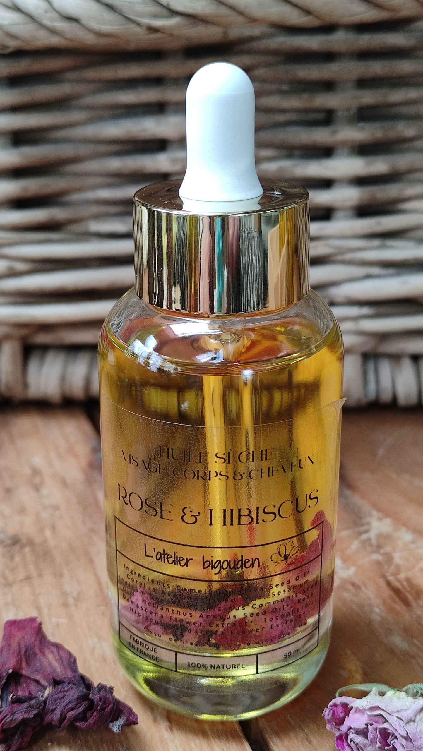 joli flacon en rondeur, transparent avec un bouchon compte-goutte doré. L'huile est jaune or avec des pétales de rose et des fleurs d'hibiscus en suspension.