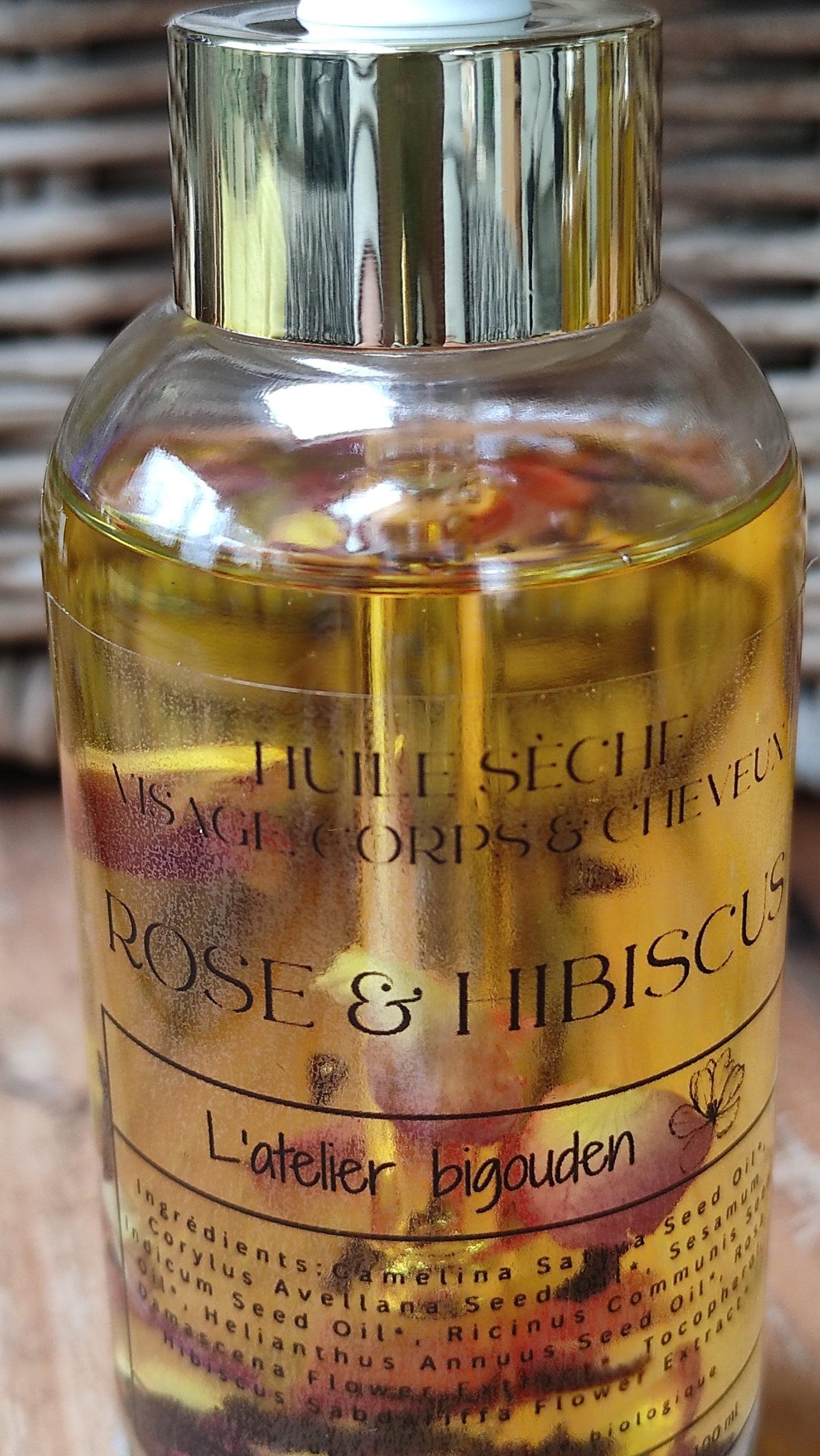 joli flacon en rondeur, transparent avec un bouchon compte-goutte doré. L'huile est jaune or avec des pétales de rose et des fleurs d'hibiscus en suspension.