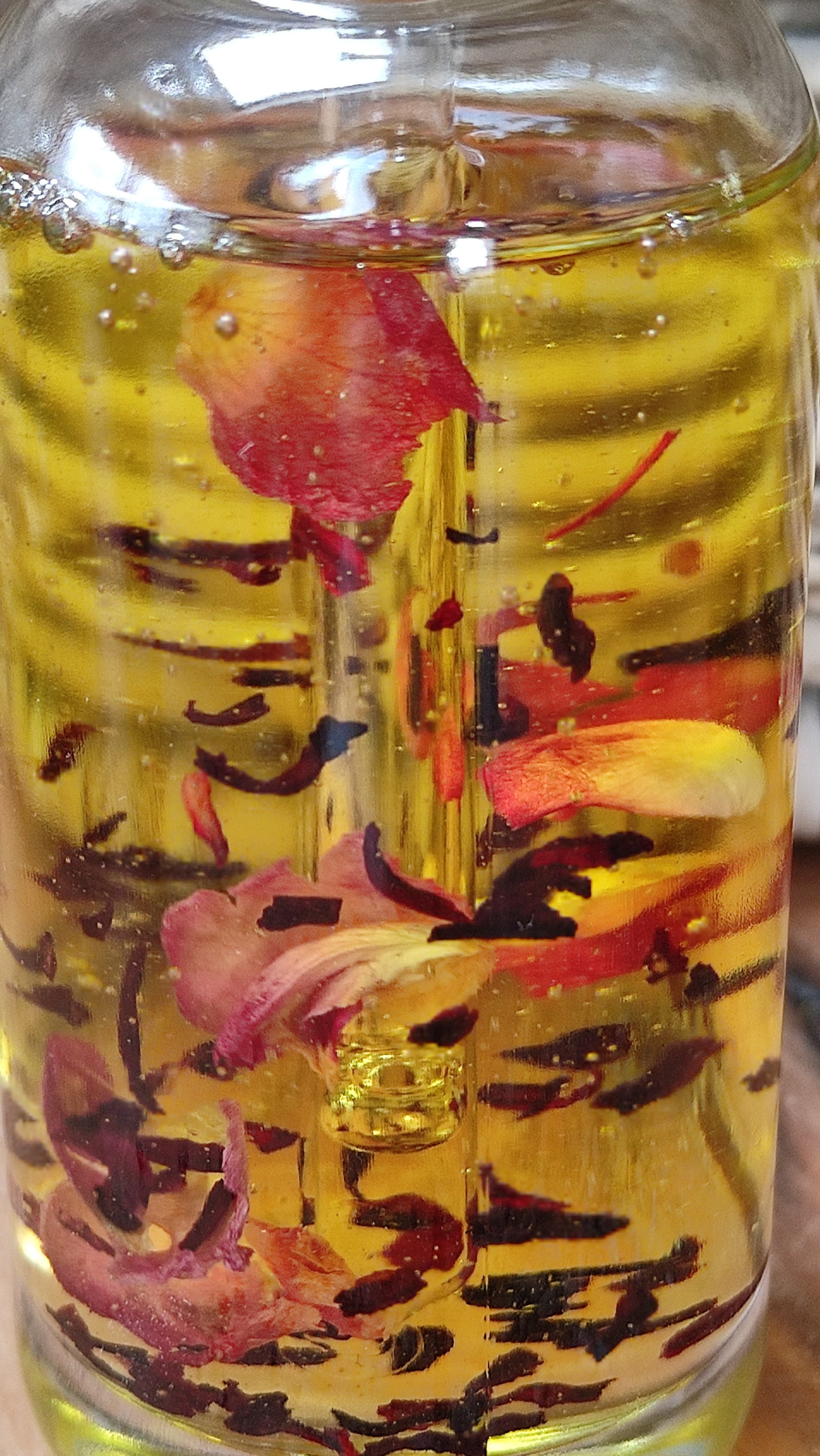 joli flacon en rondeur, transparent avec un bouchon compte-goutte doré. L'huile est jaune or avec des pétales de rose et des fleurs d'hibiscus en suspension.