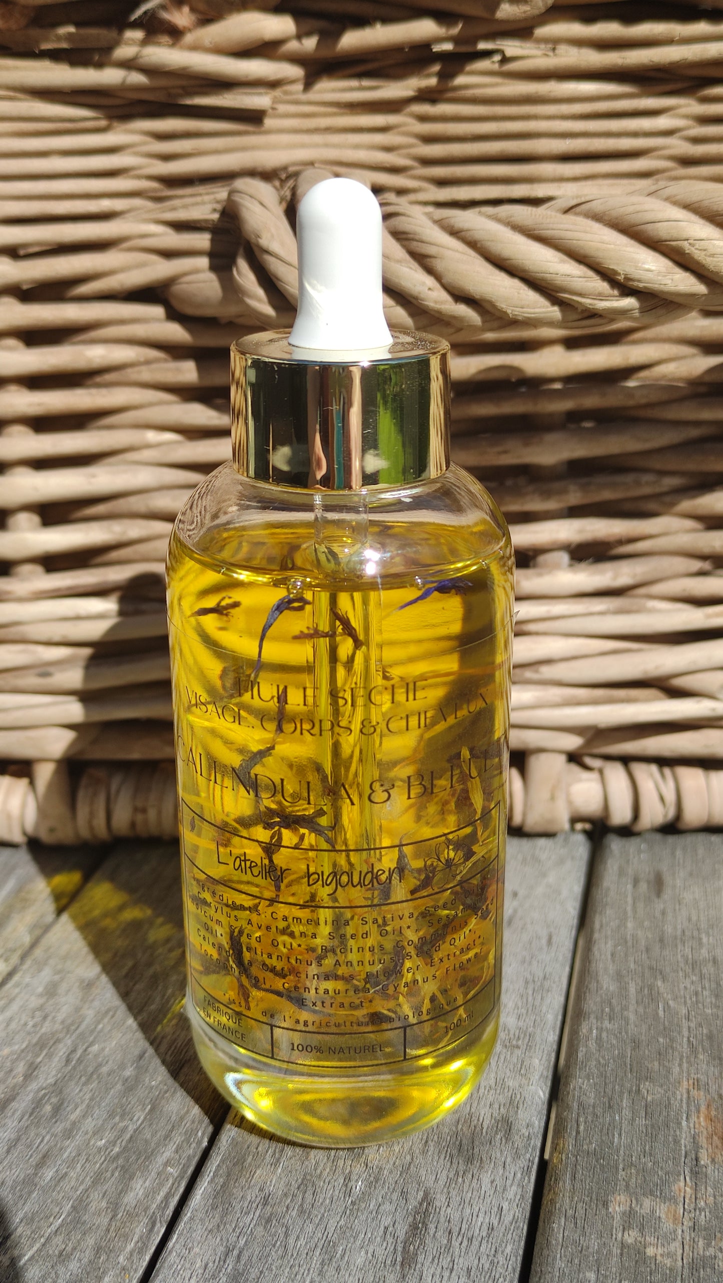 joli flacon en rondeur, transparent avec un bouchon compte-goutte doré. L'huile est jaune or avec des étale de fleurs de calendula et de bleuet en suspension.