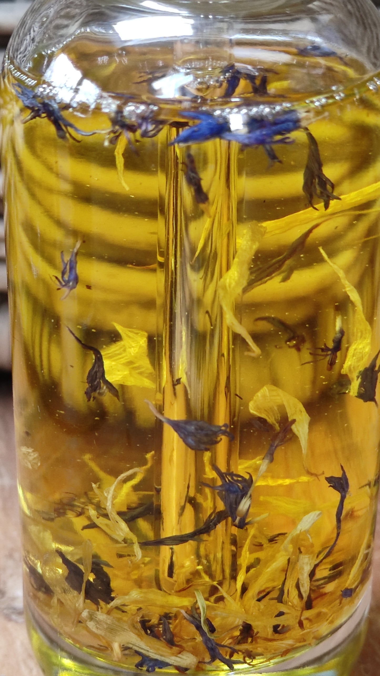 joli flacon en rondeur, transparent avec un bouchon compte-goutte doré. L'huile est jaune or avec des étale de fleurs de calendula et de bleuet en suspension.