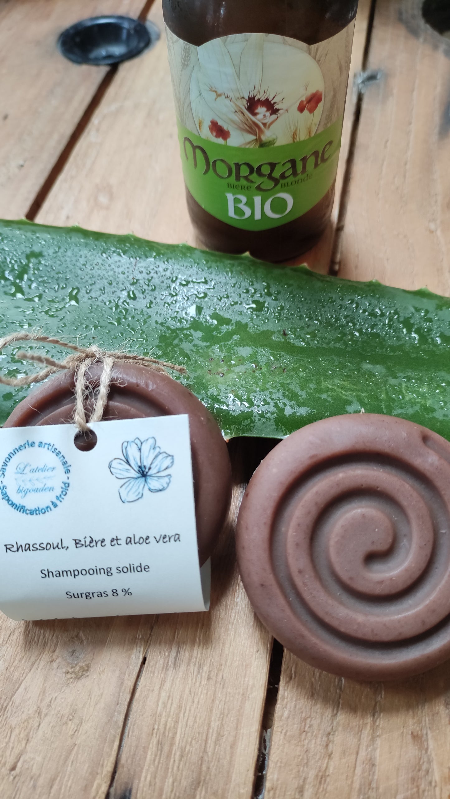shampooing naturel de forme ronde avec une spirale dessus posé sur une feuille d'aloe vera près d'une bouteille de bière