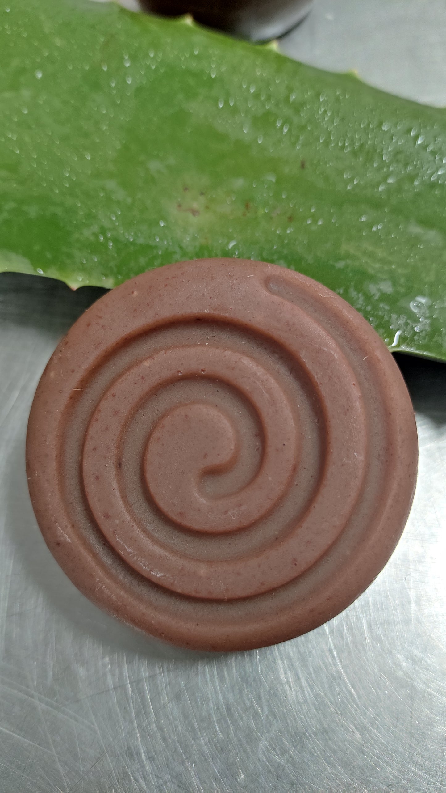 shampooing naturel de forme ronde avec une spirale dessus posé sur une feuille d'aloe vera