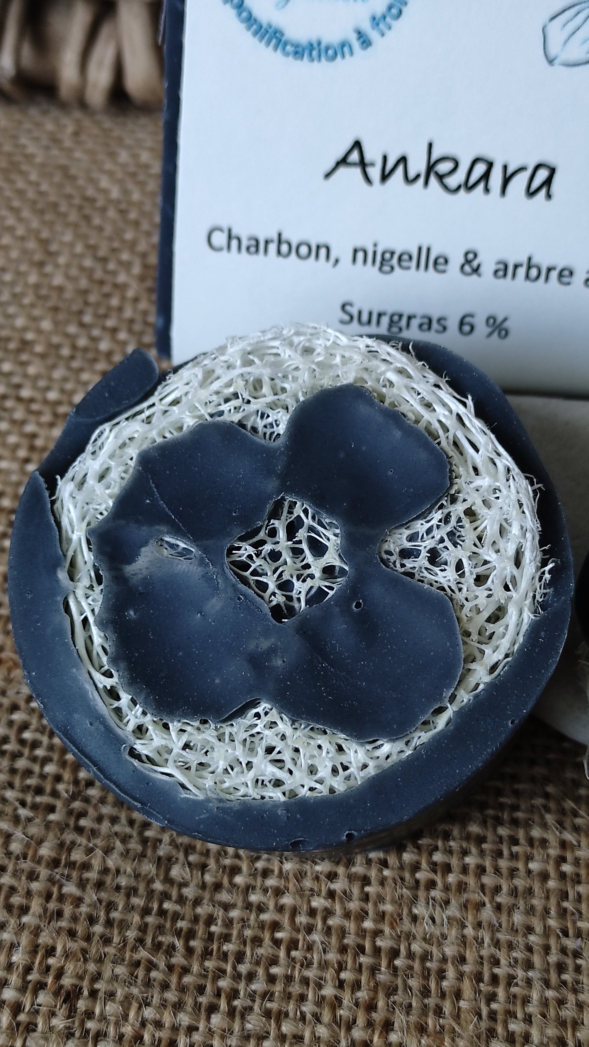 Savon naturel saponifié à froid purifiant au charbon actif, à l'huile de nigelle et huile essentielle d'arbre à thé coulé sur une rondelle de Loofah