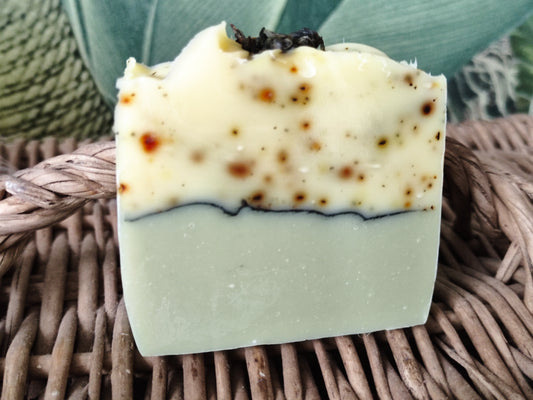 Savon artisanal saponifié à froid. Il est bicolore. La partie inférieure est vert clair et la partie supérieure blanche mouchetée de petits fragments de thé vert. une ligne de charbon sépare les deux parties. 
