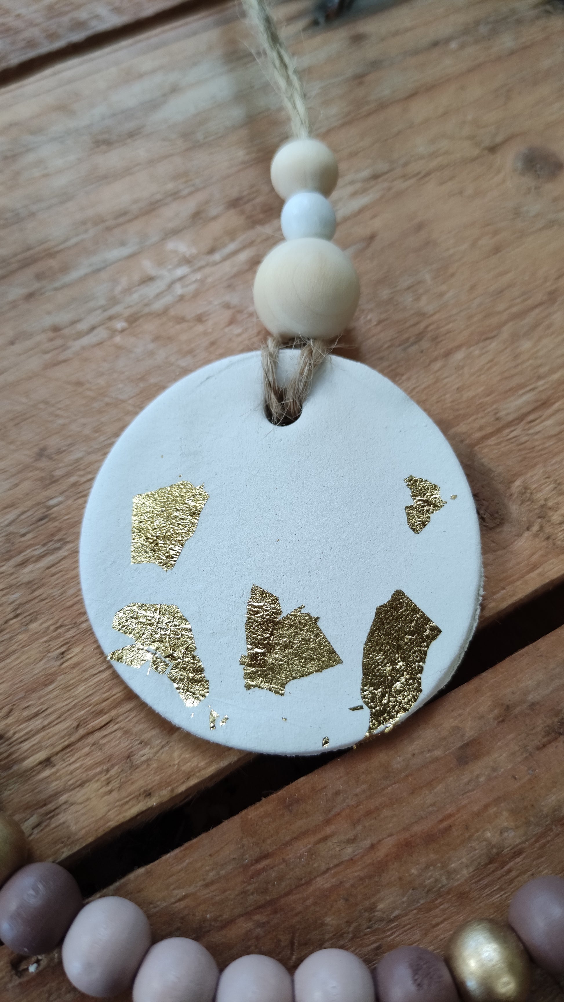 suspension ronde en argile blanche et touche de feuilles d'or soutenu par une ficelle de chanvre avec 3 perles de bois aux tons naturels