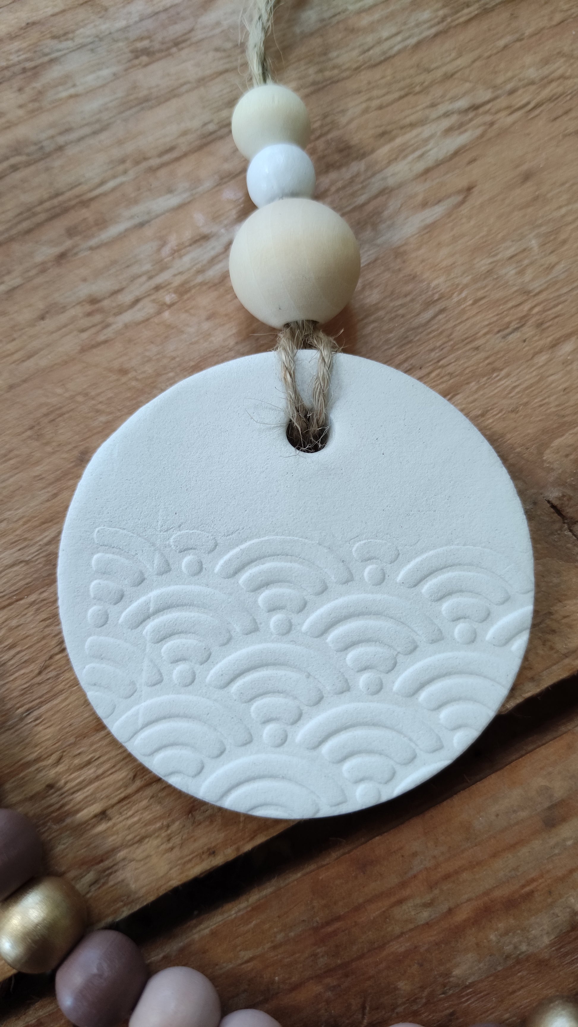 suspension ronde en argile blanche (motif vague en relief) soutenue par une ficelle de chanvre avec 3 perles de bois aux tons naturels