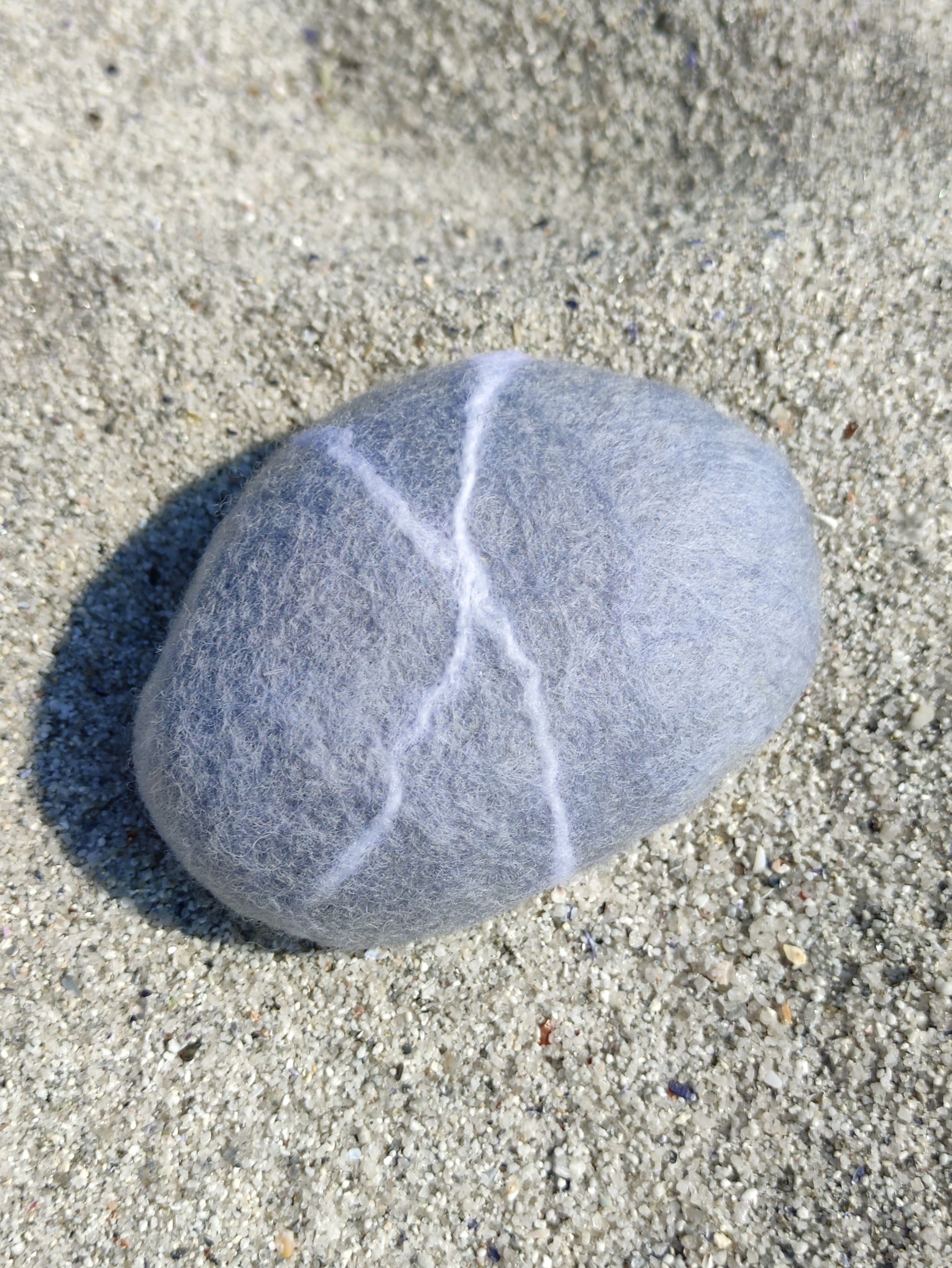 savon saponifié à froid, savon en laine feutrée imitant un galet gris posé sur le sable