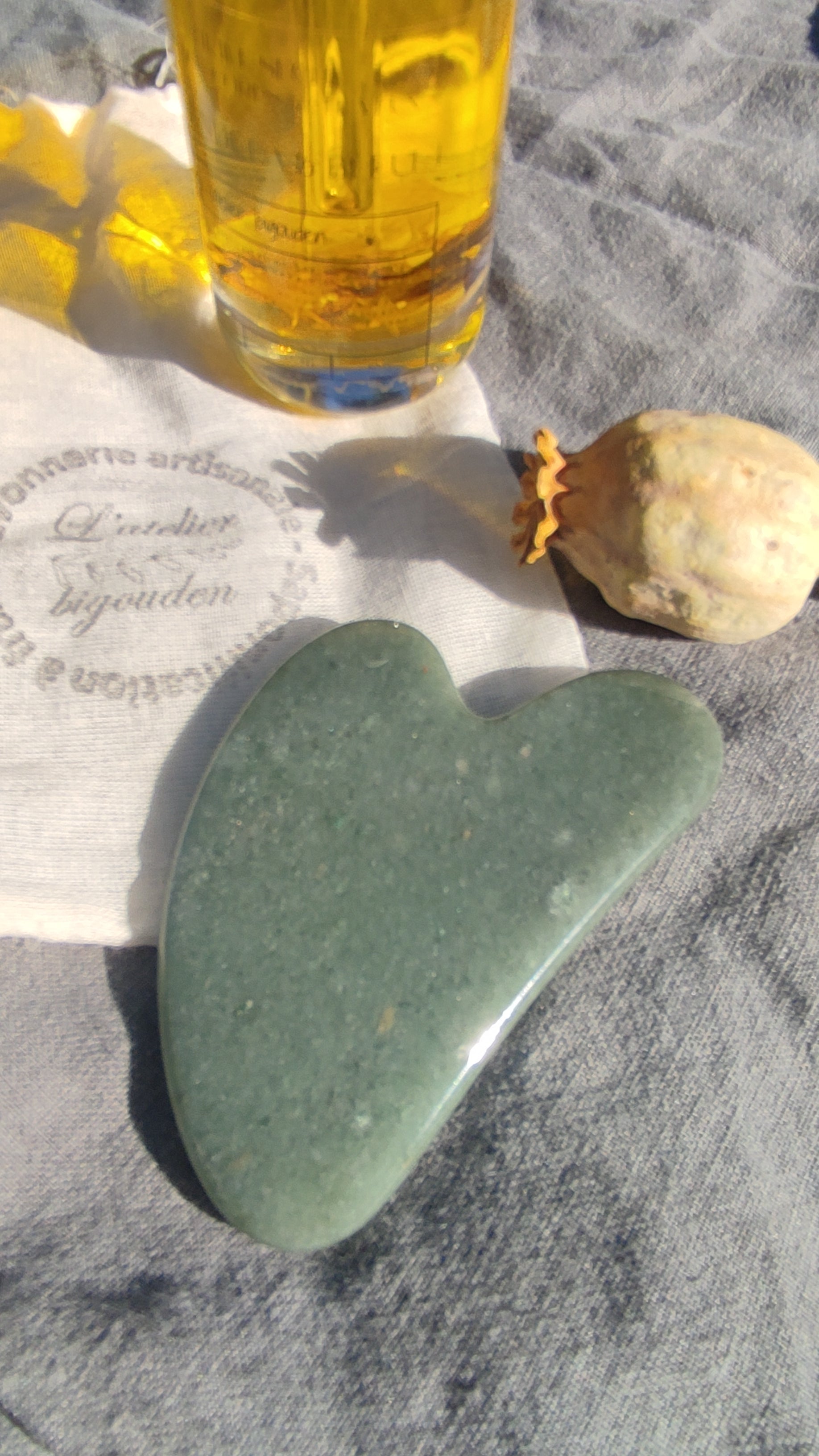 pierre plate d'aventurine en forme de coeur présentée avec une huile visage au macérât de fleurs