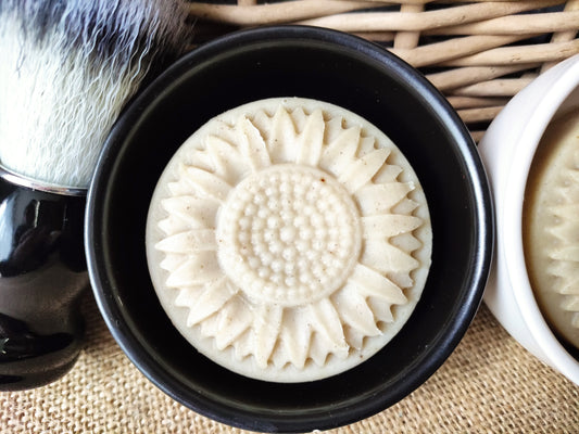 savon rond avec un motif tournesol dans un support rond en céramique avec un blaireau posé à côté